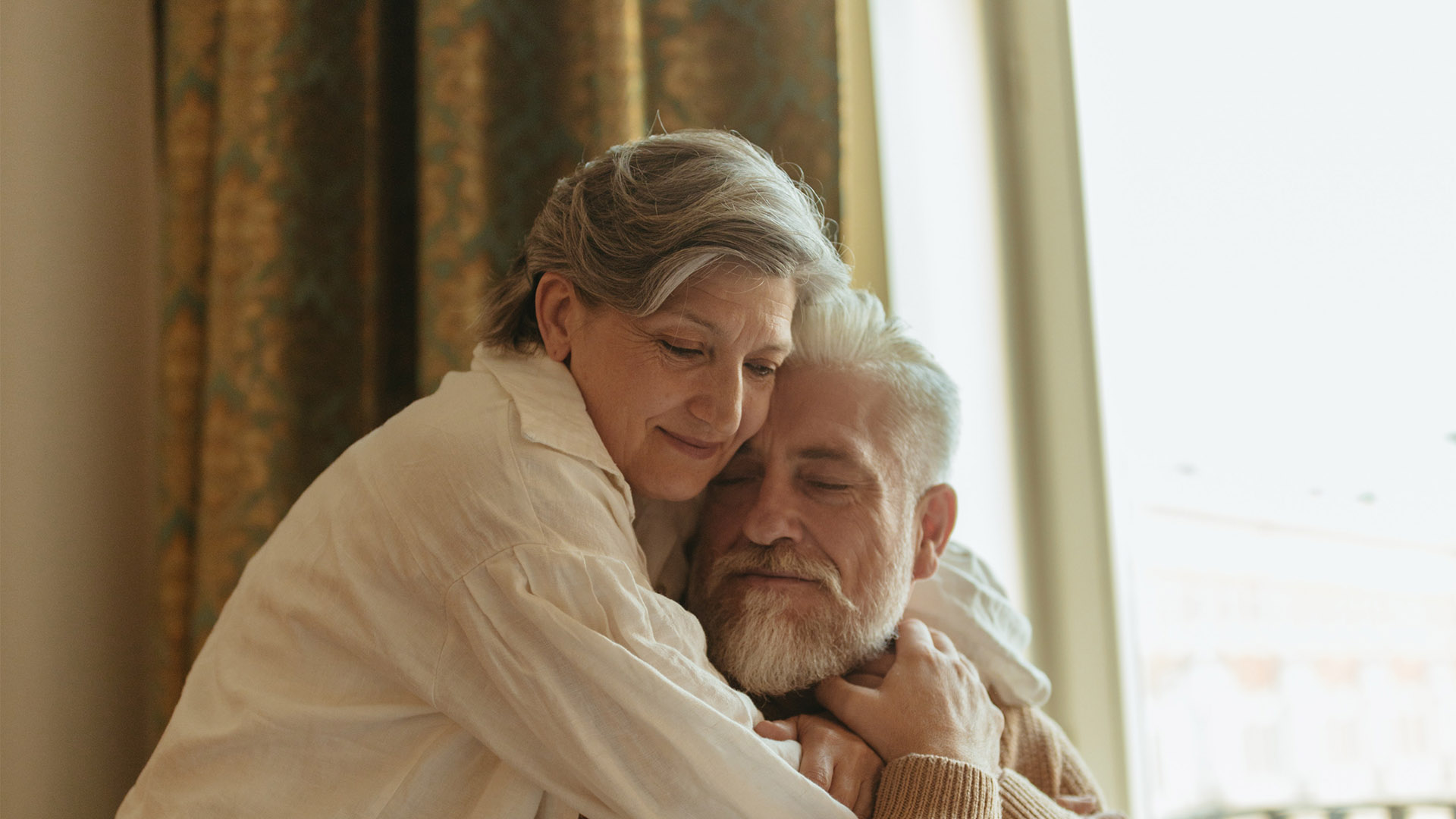 Two people embrace in sun-lit room.